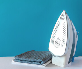 an iron with a shiny surface stands on a white ironing board with two folded kitchen towels on a...
