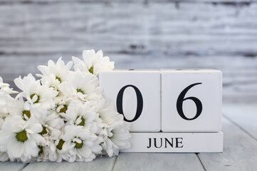 White wood calendar blocks with the date June 6th and white daisies. Selective focus with blurred...