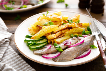 Pickled herring fillet with onion and fried potato on plate