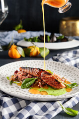 Fish Plate Restaurant Food - Grilled Salmon Steak with Vegetables Tartare. Salmon Fillet Garnished with Pesto and Citrus Sauce and Basil Leaf. Table with Kitchen Towel. Pouring Orange Sauce in Plate.