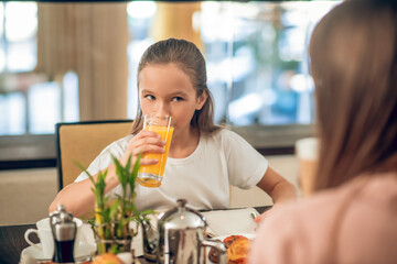 Teen girl sitting at the table and drinking orange juice