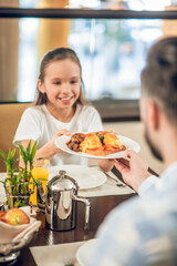Pretty teen girl taking a plate with food from her dads hands
