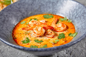 Tom Yum or Tom Yam Soup - Hot and Sour Thai Soup cooked with Shrimp. Thai Authentic Traditional Dinner. Soup in Blue Bowl on Dark Grey Table. Street Asian Food.