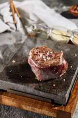 Fillet Steak - Cooking Filet Mignon Beef Steak on Hot Steak Stone with Salt and Pepper. Raw Beef Meat with Steam from Hot Stone.