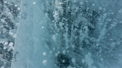 Ice, close-up, details. Cracks are visible on the transparent shiny surface. Columns of frozen methane gas bubbles go into the depths. Lake Baikal