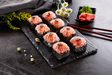 International maki sushi roll on black slate plate. Served with wooden chopstick, green wasabi and pickled ginger. Japanese set with maki sushi roll on dark stone background..