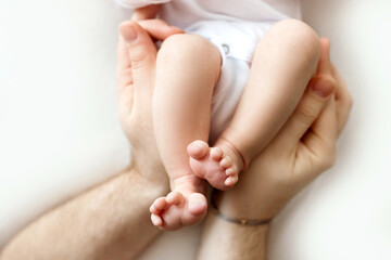 Feet of a newborn in the hands of a father, parent. Studio photography, white background. Happy family concept.