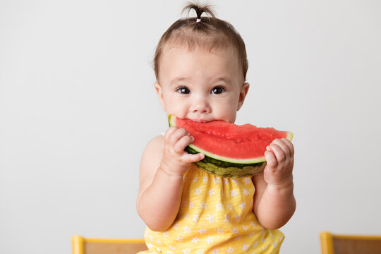 Portrait of baby girl sitting on kitchen table eating slice of watermelon