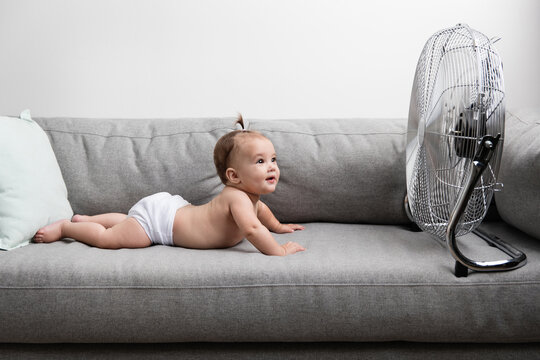 Cute baby lying on sofa facing electric fan