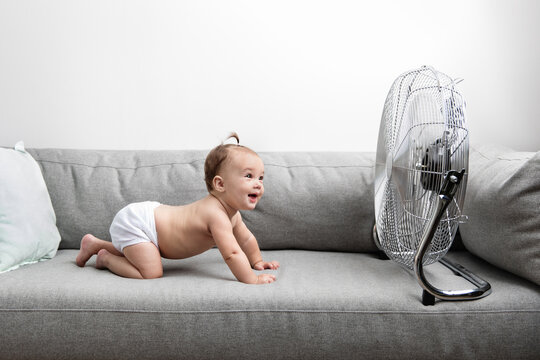 Smiling baby crawling on couch facing electric fan