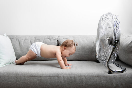 Funny baby doing pushups on couch in front of electric fan
