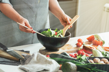 Close up photo of woman hands making fresh salad. Housewife making lunch, mixing organic vegetables with mixing spoon at kitchen with sun rays in home