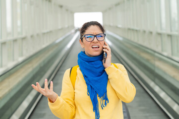 Caucasian woman stands on the escalator and is displeased talking on the mobile phone.