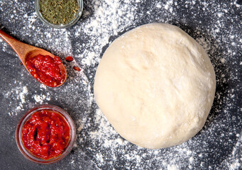 Raw pizza dough with with tomato sauce and herbs. Top view