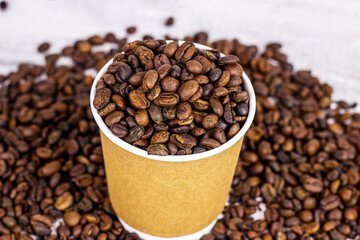 Brown cardboard disposable cup with coffee and roasted coffee beans on the table with copy space on light background. Takeaway food concept.