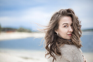 portrait of a beautiful sensual young woman, hair develops the wind, brunette with emotions, hands hair and face, seaside wind outside