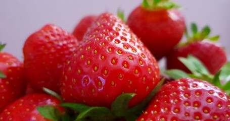 Heap of red fresh delicious strawberries with leaves in front of violet background