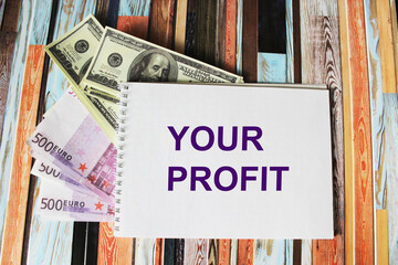 Notepad with the text YOUR PROFIT, dollars and euros lie on a colored striped background.