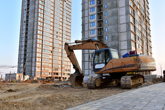 Excavator working at construction site on earthworks. Backhoe on road work and aying sewer pipes. Construction machinery for digs ground, excavating foundation. Tower cranes in action