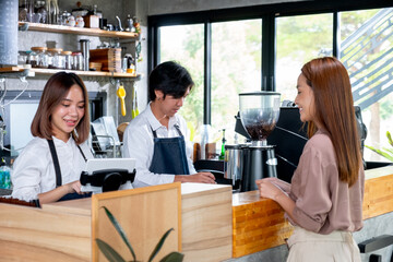 Asian barista or coffee maker receive the order from customer woman while her co-worker prepare coffee by machine. Concept of good teamwork support small business system.
