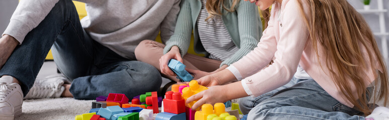 Cropped view of child and mother playing building blocks near father, banner.