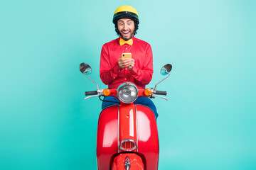 Fototapeta premium Photo of impressed brunette guy ride on bike hold telephone wear red shirt helmet isolated on teal color background