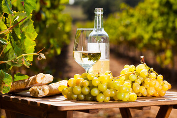 still life with glass of White wine grapes and bread on table in field