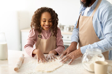 Afro man and his child daughter kneading dough on table