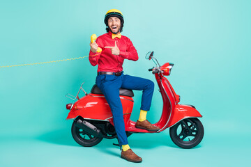Fototapeta na wymiar Full size photo of young funny smiling man riding moped point finger cord phone recommend isolated on turquoise color background
