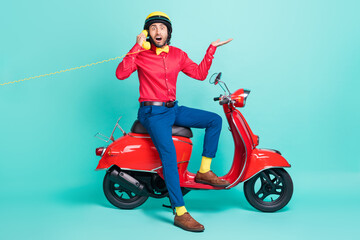 Fototapeta na wymiar Full size photo of young shocked amazed man sit moped talking on telephone isolated on turquoise color background