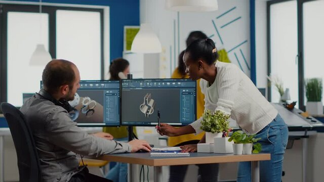 Diverse team of engineers working on computer at mechanical piece design cad sharing ideas about industrial project using dual displays setup. Black manager analysing 3D gears on CAD software.