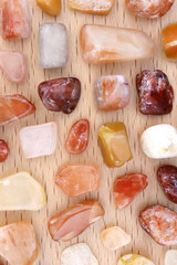 Red silk jade rare jewel stones texture on light varnished wood background. Place for text.