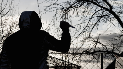 Silhouette of a man with a sharp knife against the evening sky, a criminal with a weapon outdoor