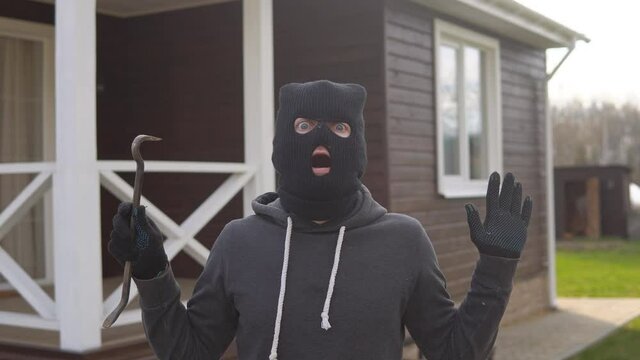 Portrait of thief in black balaclava and gloves raising hands up. Masked robber being arrested. Get Caught Concept.