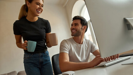 Young woman brings a cup of coffee to her boyfriend while he is working