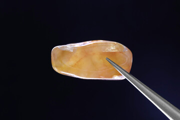 Red silk jade jewel texture in tweezers on black background. Macro closeup.