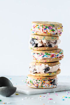 Close Up Of A Stack Of Homemade Black Cherry Ice Cream Sandwiches With Sprinkles And An Ice Cream Scoop On The Side.