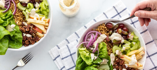 Two Waldorf salad bowls with a creamy dressing and a hand holding a fork for eating.