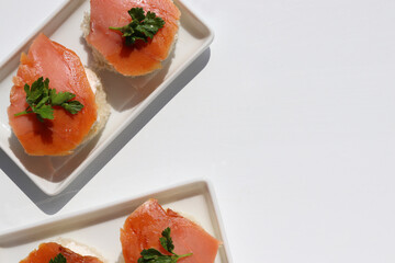 Smoked salmon canapes on white bread with cream cheese and parsley. Sandwich with salmon on white background. Top view, copy space
