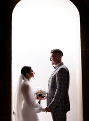 Side view of beautiful newlyweds holding hands and looking at each other on a background of white arches. Concept of wedding couple