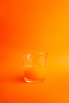 half glass of orange juice on orange background