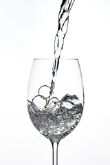 golden rings in a glass goblet with a stream of water on a white background