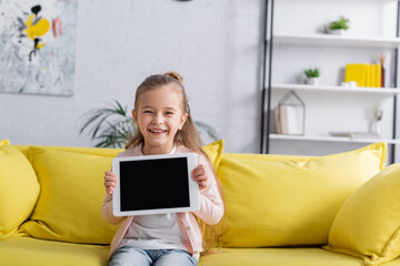Smiling kid holding digital tablet with blank screen on couch.