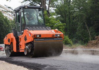 large orange roller in the process of rolling hot asphalt. paving works. Improvement of the city. Equipment for road construction and repair. rent,  leasing