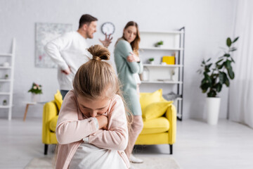 Displeased kid with crossed arms standing near father quarreling with mother.