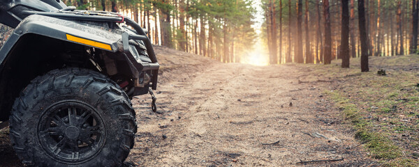 Clode-up side of ATV awd quadbike motorcycle profile view dirt country forest road beautiful nature morning sunrise landscape. Offroad travel adventure trip expedition. Extreme recreation activity
