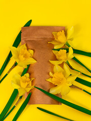 Brown kraft paper pouch bag mockup coffee beans and yellow daffodil flowers on pastel background top view. Packaging for food product template.Pack with clasp for tea leaves,weight flat lay copy space