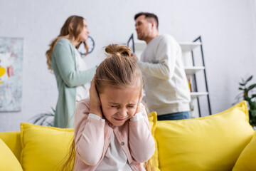 Girl covering ears near parents quarrelling at home.