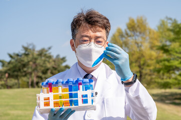 Portrait of a middle-year Asian male scientist wearing a white lab gown and gloves and holding an...