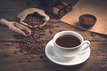 Coffee in a white ceramic cup on a wooden background with coffee beans.